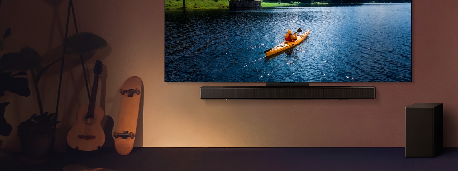 LG TV et Soundbar montés sur un mur avec un caisson de basse sur le sol à droite. La TV affiche une personne en train de faire du kayak sur un lac, tandis que des ombres couvrent le mur.