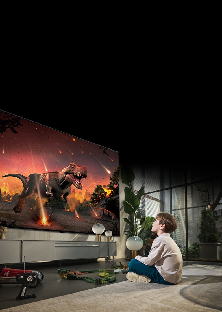 Une image d'un petit garçon assis par terre devant le LG OLED G2 de 97 pouces. Il regarde avec admiration un film de dinosaure hyperréaliste sur grand écran.