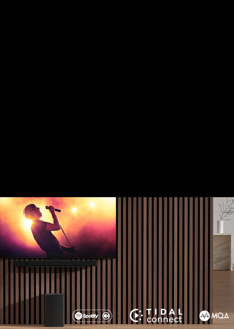 Le LG OLED C est placé sur le mur, en dessous la barre de son LG SC9S est placée sur un support exclusif. Le caisson de basses est placé en dessous. Le téléviseur affiche une scène de concert.