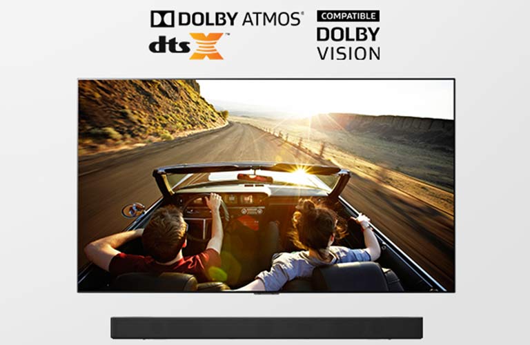 Téléviseur et barre de son ensemble en pleine vue. Le téléviseur montre un couple dans une voiture décapotable sur la route qui se dirige vers le coucher du soleil. 