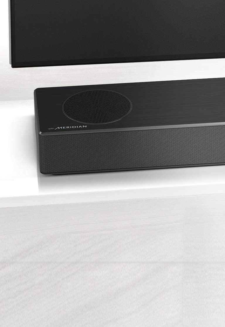 Gros plan de la barre de son LG sur le côté gauche, avec le logo Meridian en bas à gauche. Le côté inférieur gauche du téléviseur est également visible. 