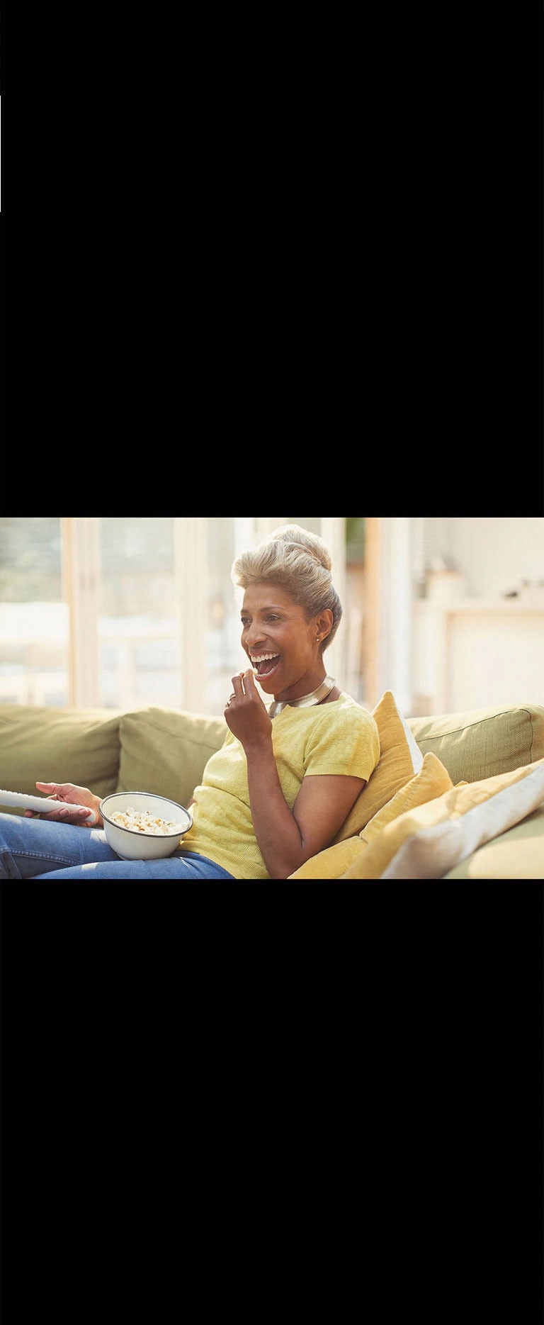 Une femme regarde le téléviseur – tenant une télécommande. Elle mange également du pop-corn.