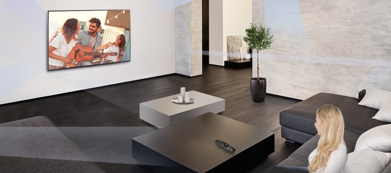 Une femme dans un grand salon à la décoration minimaliste en train de regarder des gens jouer sur un téléviseur