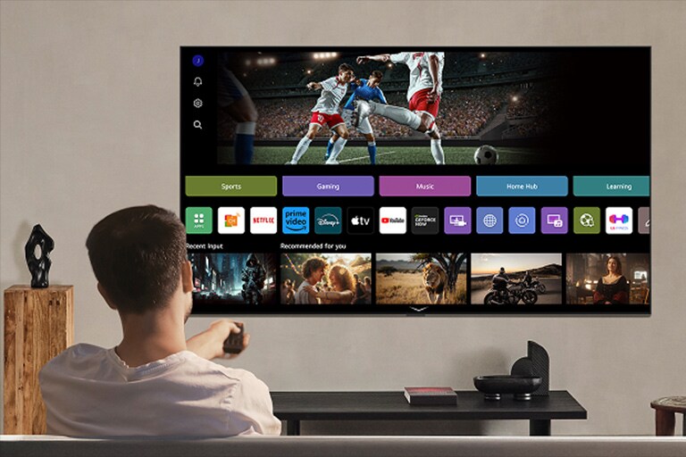 Une personne sur le canapé tenant une télécommande. Une LG AI TV sur le mur avec LG webOS à l’écran.