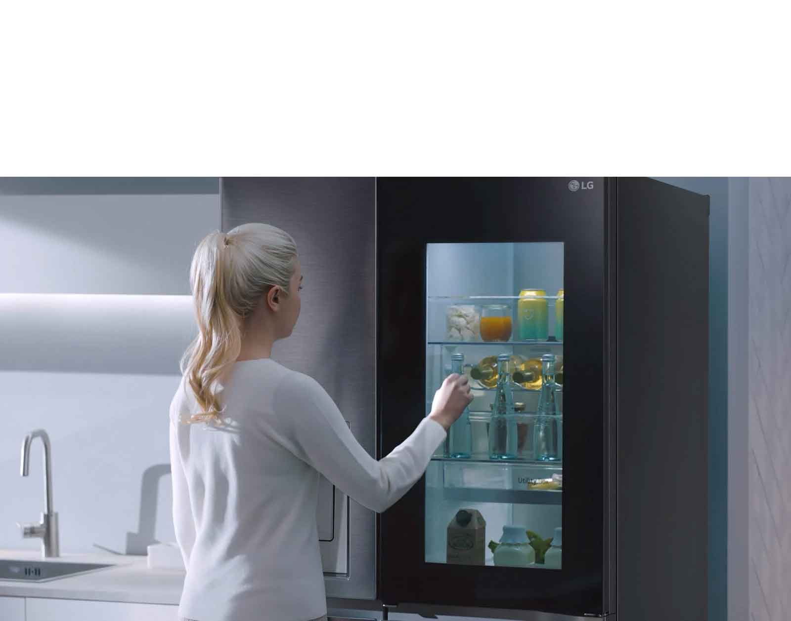 Une vidéo montre une femme qui s’approche de son réfrigérateur InstaView et frappe deux fois. L’intérieur du réfrigérateur s’allume et elle peut voir son contenu sans ouvrir la porte. La vue effectue un zoom avant pour présenter les boissons posées sur la porte, puis un zoom arrière pour voir la femme de derrière alors qu’elle ouvre la porte et prend une boisson.