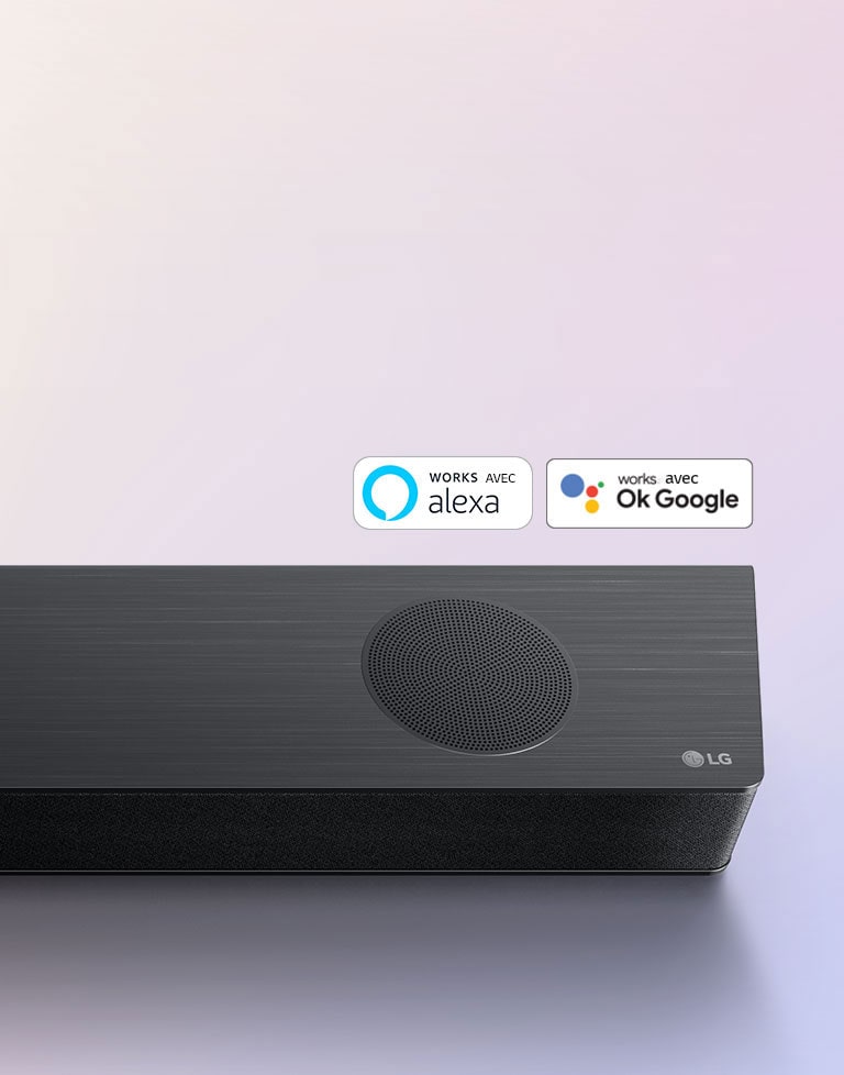 La barre de son LG est installée au sol, affichant le logo LG dans le coin droit de la barre de son. Le logo Alexa et les logos OK GOOGLE sont placés sur la barre de son.