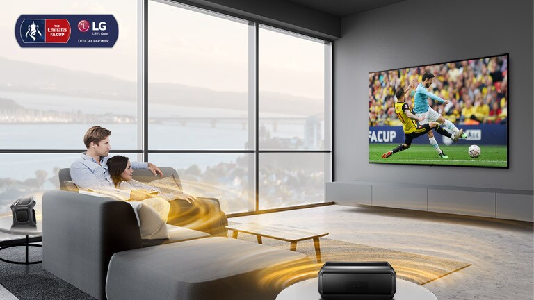 Homme et femme regardent un match de sport dans le salon avec des haut-parleurs bleutooth