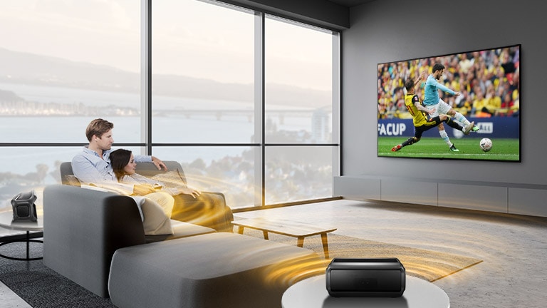 Homme et femme regardent un match de sport dans le salon avec des haut-parleurs bleutooth