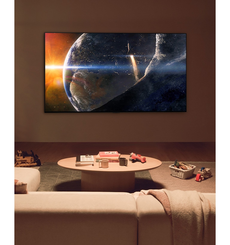 Une famille est assise sur le sol d’un salon faiblement éclairé, à côté d’une petite table, et regarde un téléviseur LG fixé au mur, qui montre la Terre vue de l’espace.