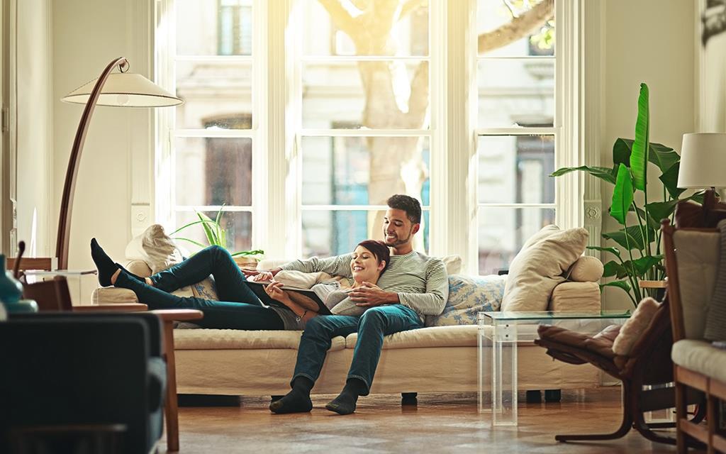 A couple is in a family living room reading a book on the sofa