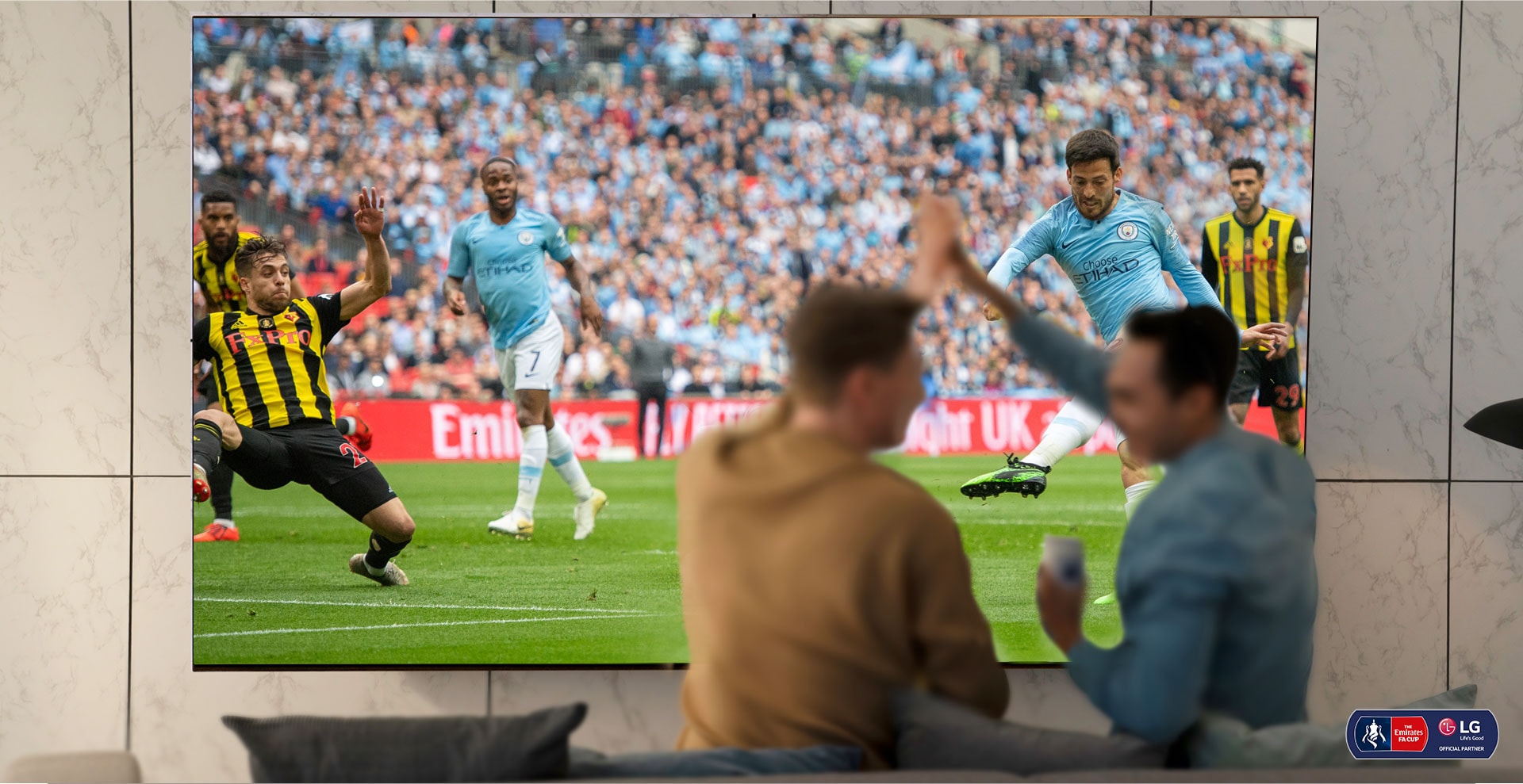 Deux hommes applaudissent en regardant un match de football sur un téléviseur NanoCell dans un salon. La technologie NanoCell est illustrée par une amélioration de l’image en dessous du téléviseur.
