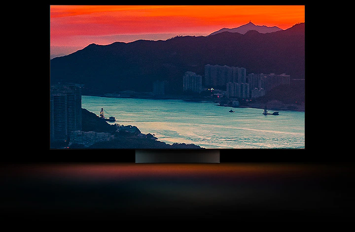 La vue aérienne d’une ville côtière, avec une circulation sur un pont et un soleil couchant, apparaît en plein écran. Elle est recadrée et affichée sur un écran de téléviseur LG OLED avec les couleurs d’origine inchangées.