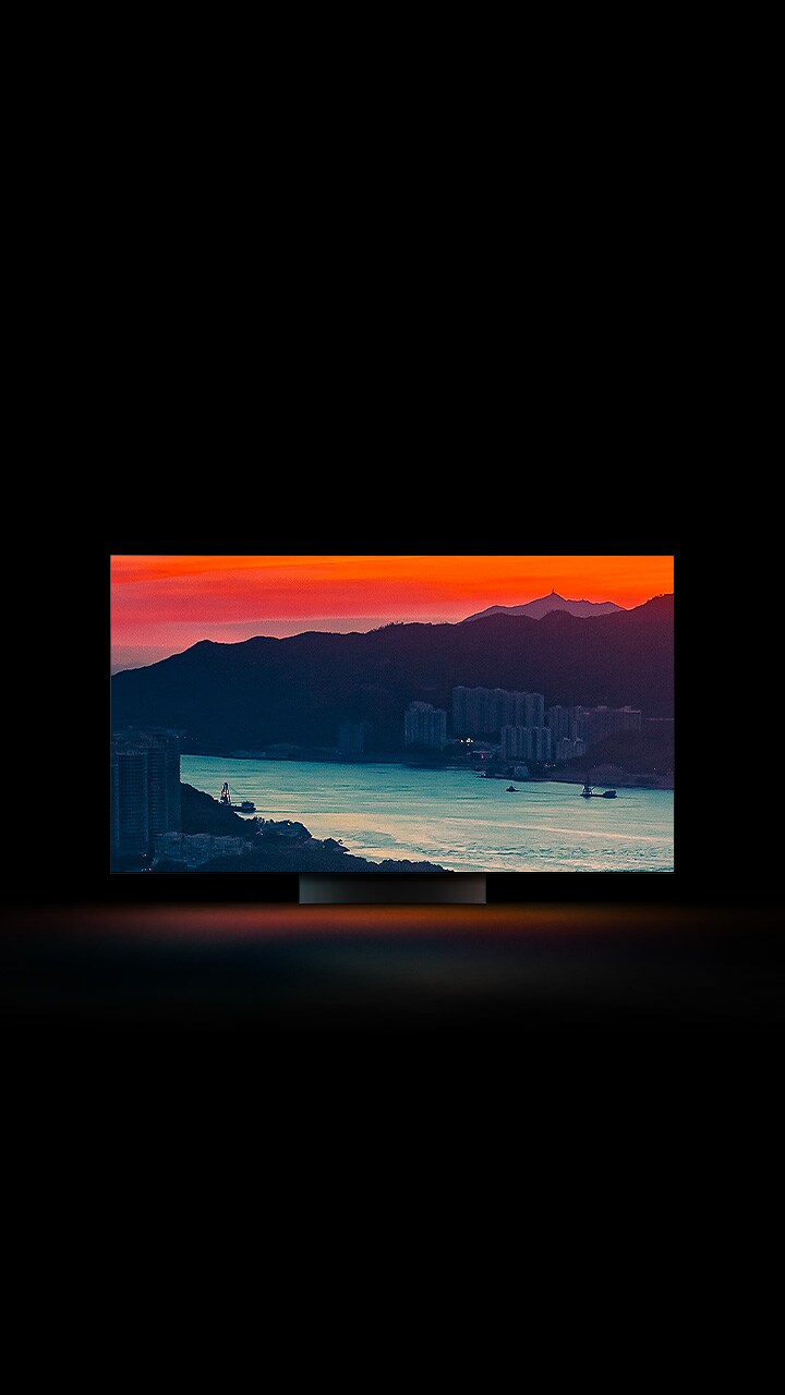 La vue aérienne d’une ville côtière, avec une circulation sur un pont et un soleil couchant, apparaît en plein écran. Elle est recadrée et affichée sur un écran de téléviseur LG OLED avec les couleurs d’origine inchangées.