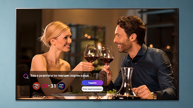 Мъж и жена вдигат наздравица с чаши на телевизионния екран, докато се показват известия за спортни събития