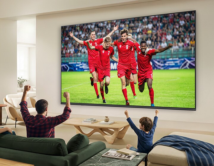 LG QNED evo AI QNED80 Mini LED Ultra Big TV е монтиран на стената в светла всекидневна и показва футболен мач с ярки цветове.