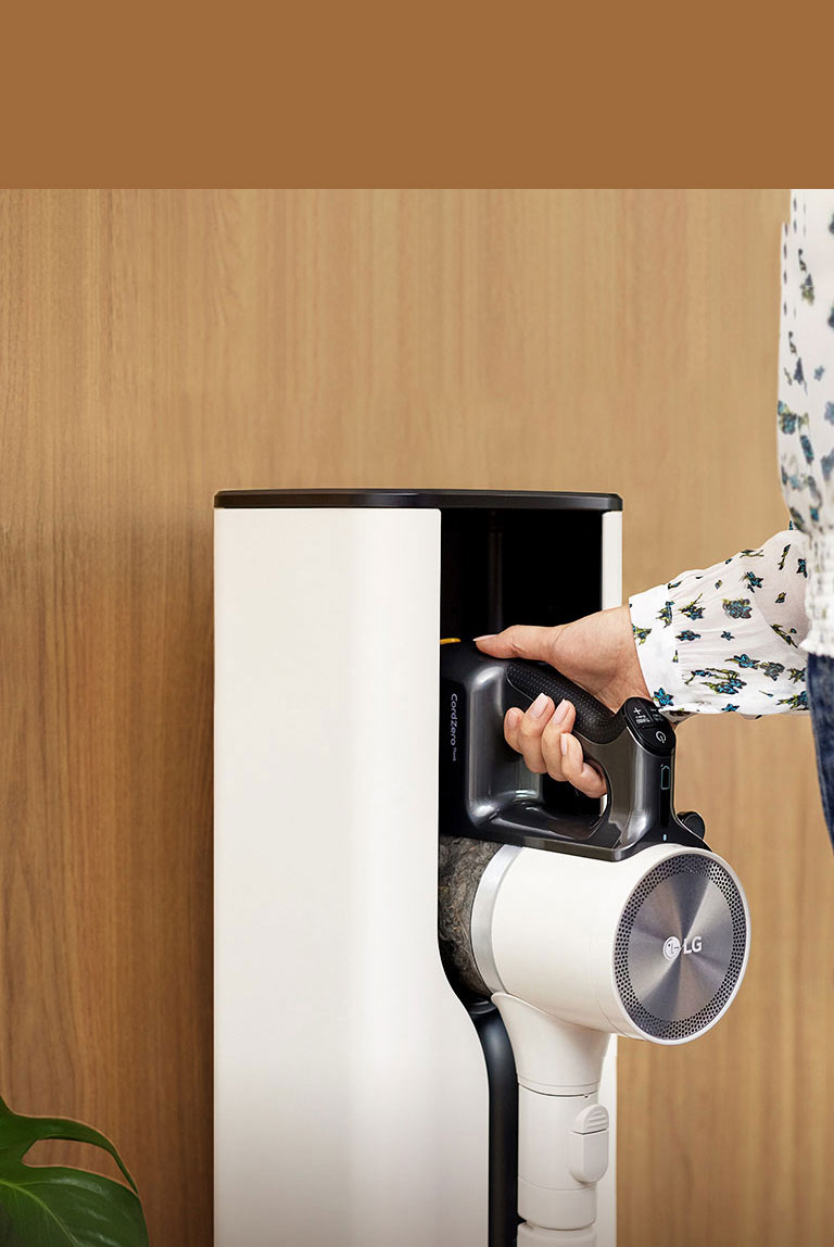A woman is putting in a Cordzero™ Vacuum cleaner in a docking station.