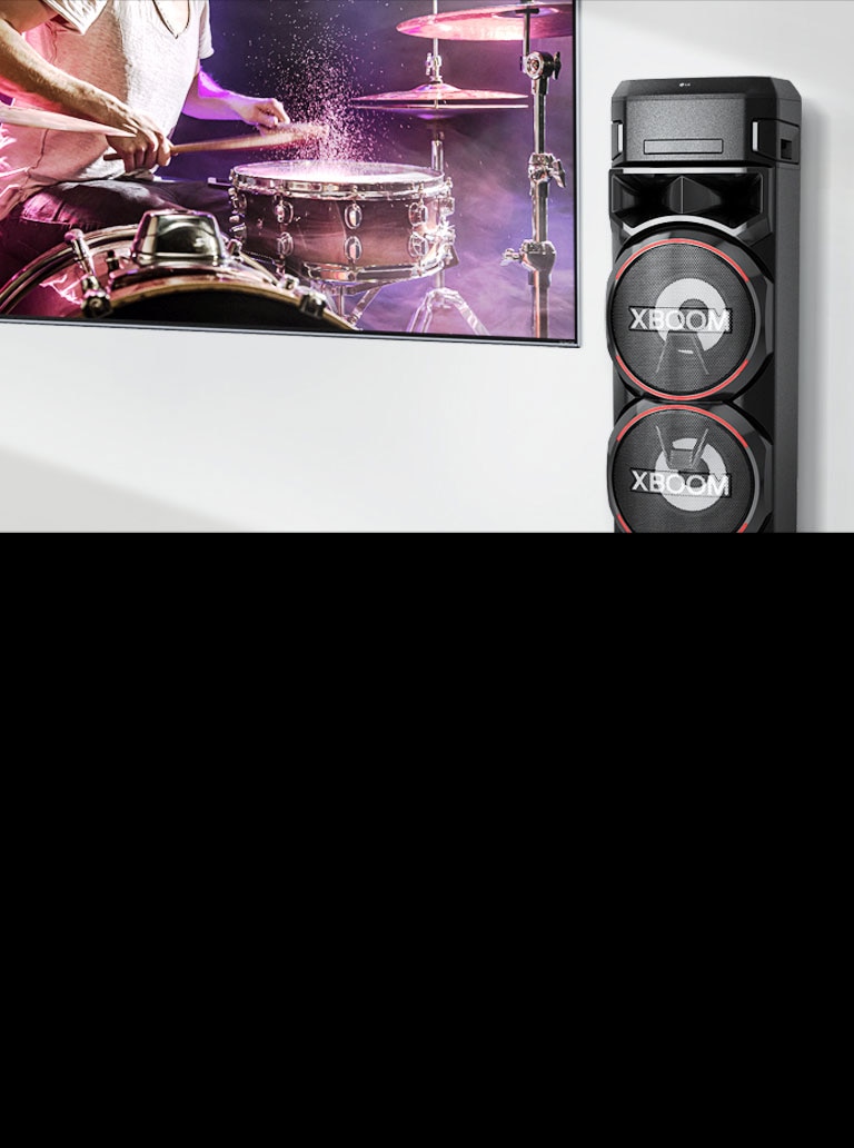 На стената е окачен телевизор, а вдясно от него има LG XBOOM.