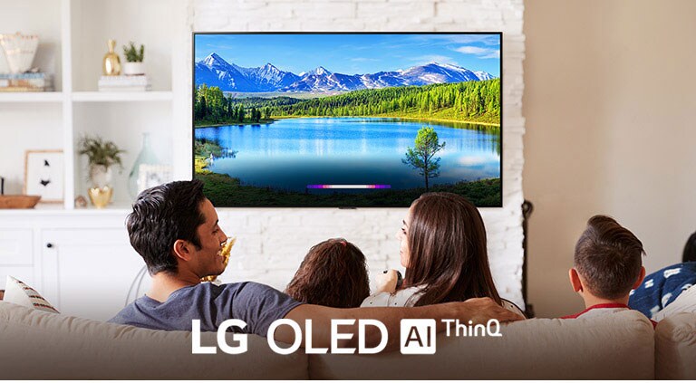 Семейство в ярко осветена всекидневна, което гледа пейзаж на монтирания на стената телевизор