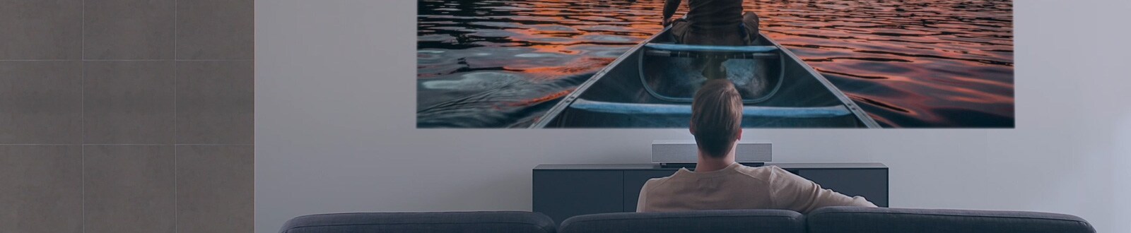 Мъж гледа филм на голям и светъл екран от LG CineBeam
