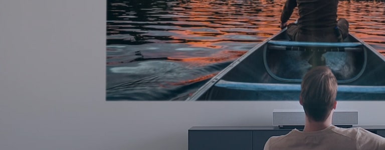 Мъж гледа филм на голям и светъл екран от LG CineBeam