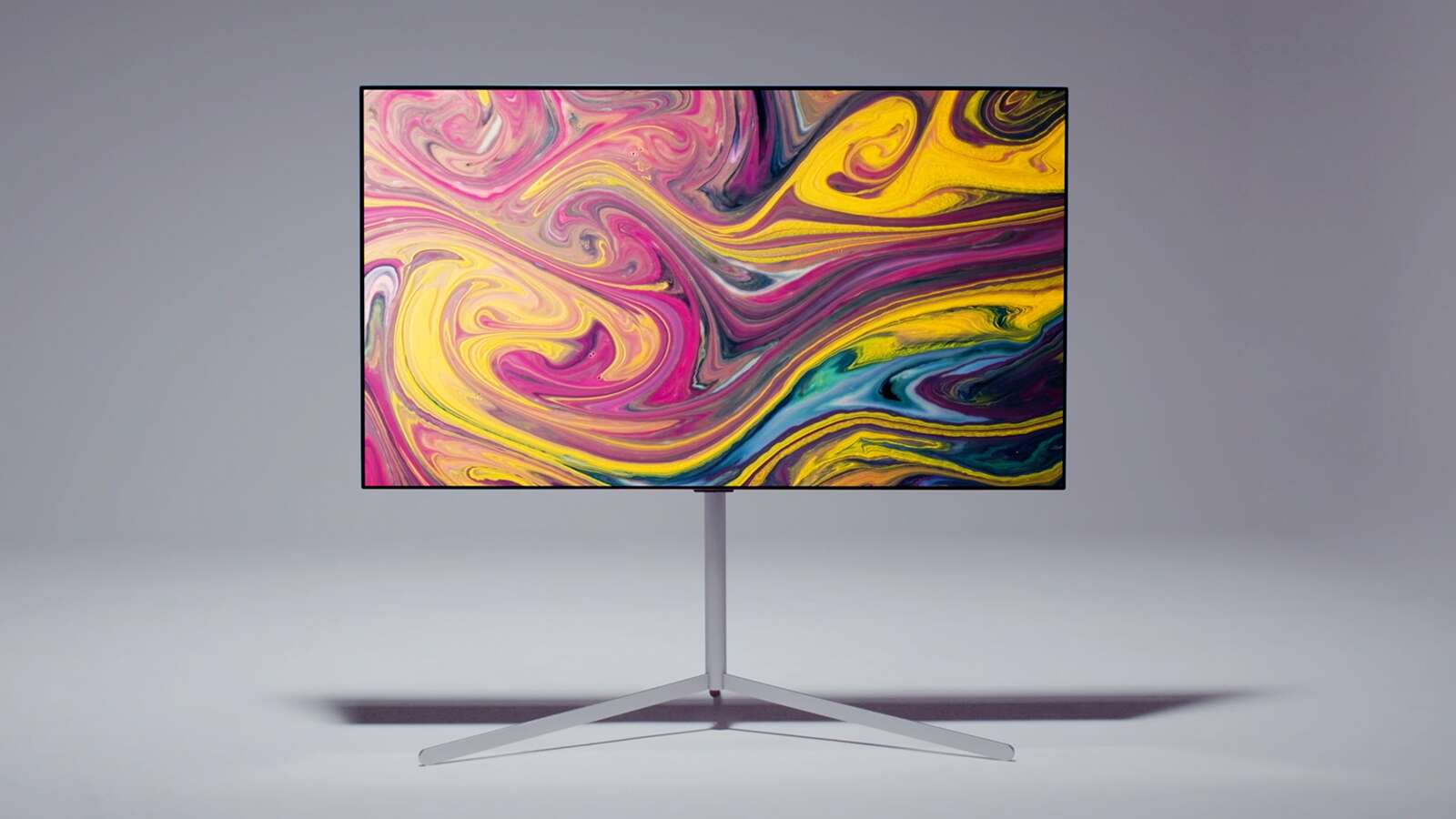 Две ръце с бели ръкавици държат колоната на стойка Gallery, като едната ръка е близо до горния край, а другата ръка е близо до долния край. Основата е поставена върху съединяващата скоба и са показани различните прорези, за да се види как може да се регулира височината на стойката. За фиксиране на стойката се използва винт. След това основата се поставя върху долния край на колоната и се завинтва, за да се прикрепи. Телевизорът се монтира върху свързващата скоба, като се подравнява с отворите върху скобата и се затяга с винта. Разклонителят с няколко гнезда, рутерът и телевизионната кутия се монтират към свързващата скоба. Кабелите се събират наедно и се прибират, а приемниците се поставят в краката на стойката. Поставен е капак, за да се скрият някои от кабелите, а камерата се отдалечава, за да покаже красив телевизор LG и стойка Gallery.