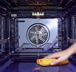 Изображение на избърсване на вътрешността на фурната с кърпа.