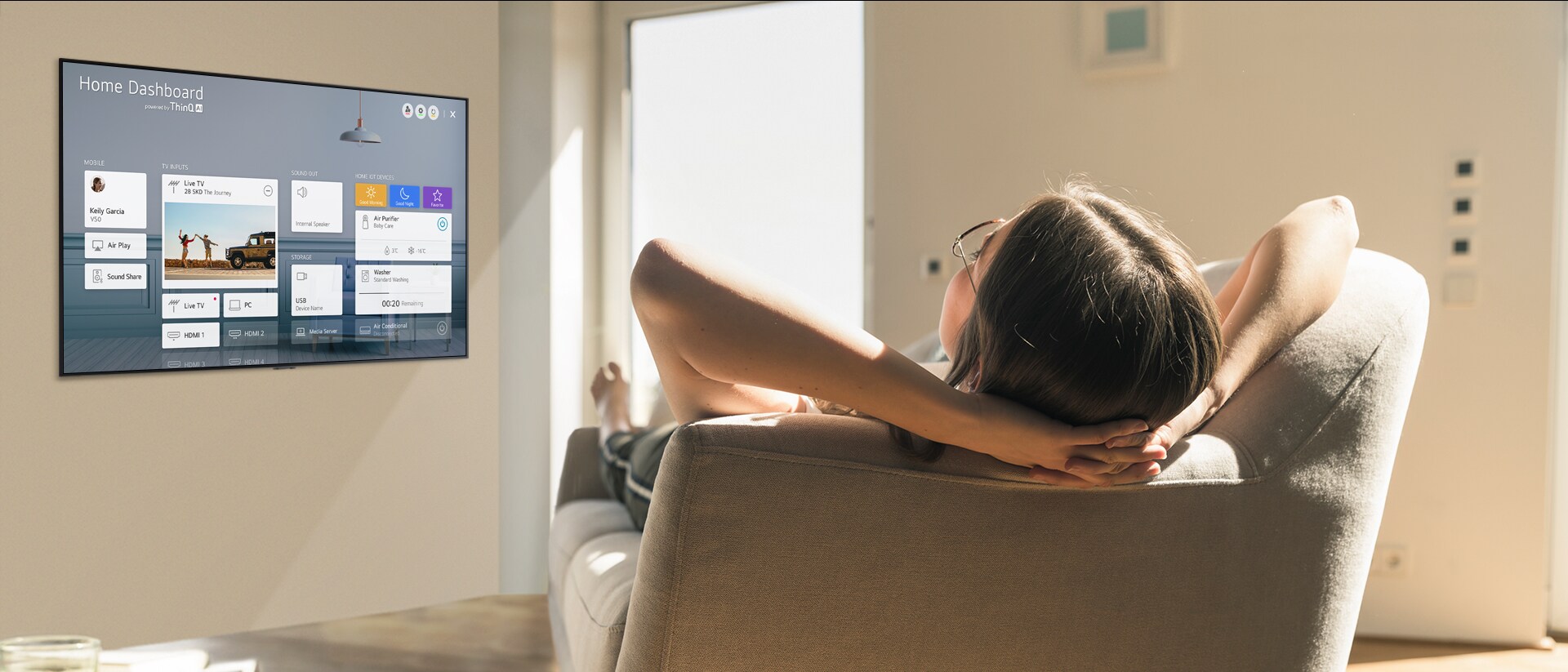 Жена лежи на дивана и казва на телевизора да намали температурата, а на телевизионния екран се вижда таблото за управление на дома.