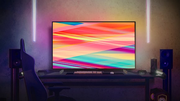 LG OLED C2 е в топло осветена стая през нощта с дивани, много възглавници, лампа, нощно шкафче и растение