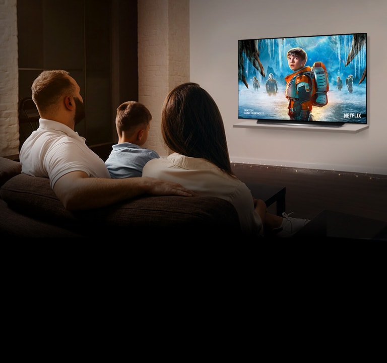 Um casal sentado em um sofá na sala de estar assistindo à série PERDIDOS NO ESPAÇO 2 na TV