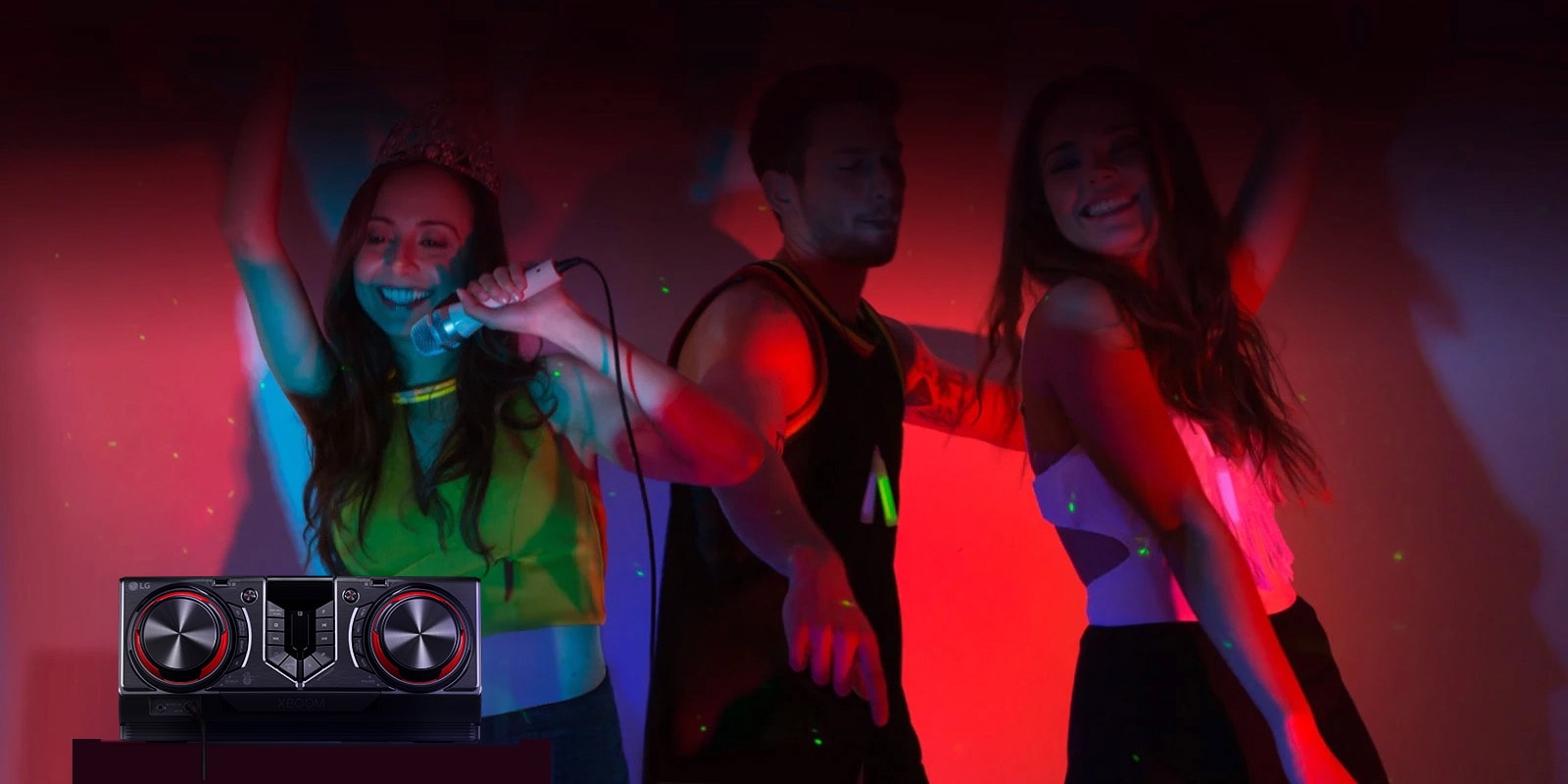 La imagen muestra una fiesta con luces de neón rojas. La gente disfruta de la música; uno de ellos sostiene un micrófono mientras los otros dos bailan. En el lado izquierdo de la imagen hay una mesa con un receptor colocado encima.