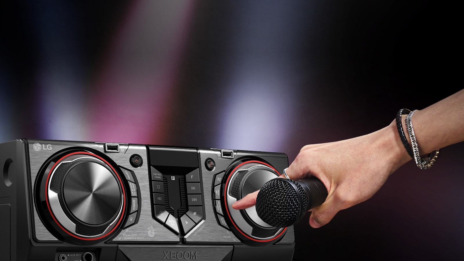 La imagen muestra un fondo borroso. En el lado izquierdo de la imagen, hay un primer plano de la vista lateral del receptor, con una mano sosteniendo un micrófono. El dedo índice se extiende para presionar el botón de karaoke.