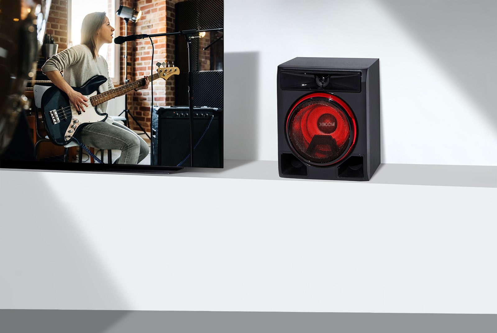 La imagen muestra un primer plano de una larga mesa de televisión blanca. A la izquierda, un televisor LG muestra una escena de un concierto de guitarra. En el lado derecho del televisor, se coloca un altavoz sobre la mesa.