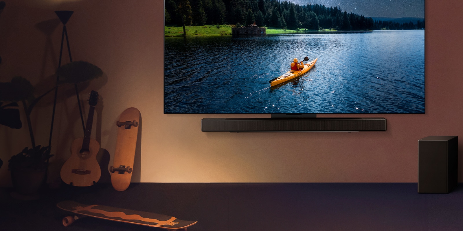 LG TV y Soundbar montadas en una pared y una bocina subgrave en el piso a la derecha. En la TV se muestra a una persona en un kayak en un lago y sombras suaves caen en cascada sobre la pared.