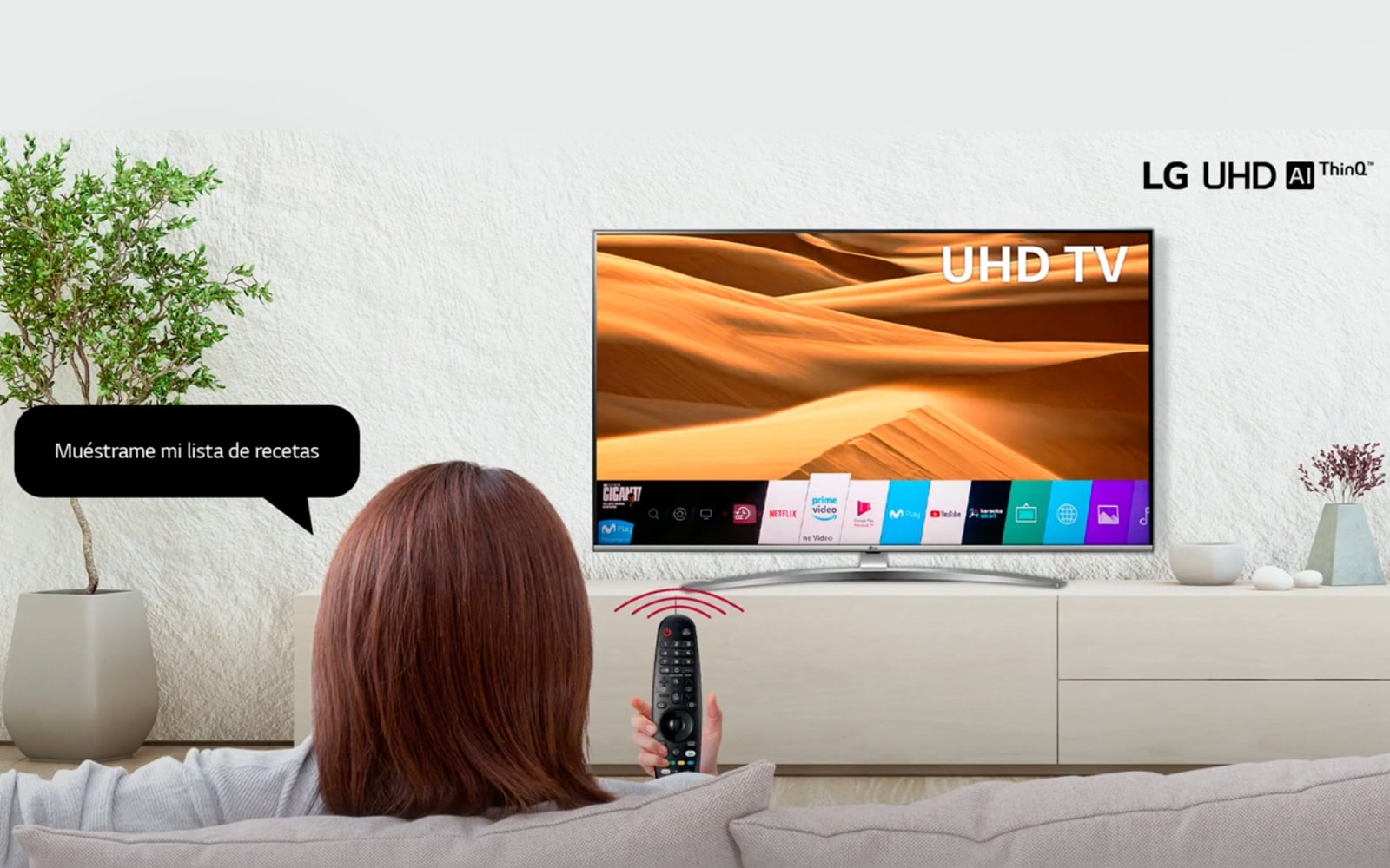 Una mujer sentada en us sofá utiliza el Google Assistant de un TV LG UHD con su Magic Remote.
