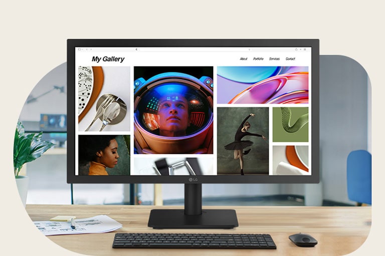 Monitor LG Full HD de 22 pulgadas en un moderno escritorio de oficina que muestra una colorida página web de galería de fotos, rodeado por un teclado, mouse, taza de café y auriculares en un espacio de trabajo luminoso.