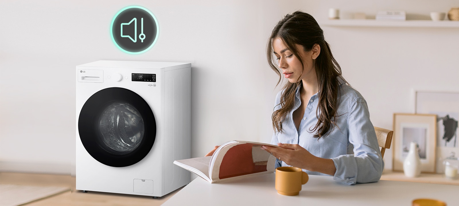 Hay una lavadora en la sala y una mujer está sentada en una silla leyendo un libro.