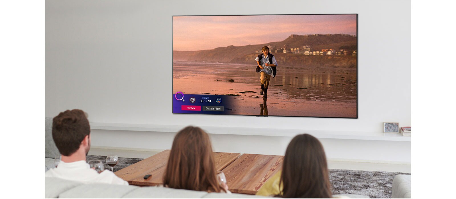 Tres personas mirando la pantalla de TV que muestra una escena de una película de fantasía con un Alerta de deportes