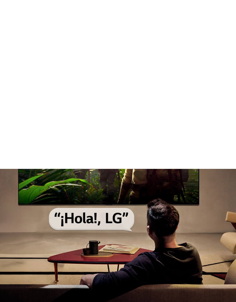 LG OLED evo AI C6 con Reconocimiento de Voz de Campo Lejano se activa mediante un comando de voz cuando una persona sentada en una habitación dice “Hola, LG” hacia el televisor, indicando una interacción por voz manos libres dentro de la interfaz del televisor.
