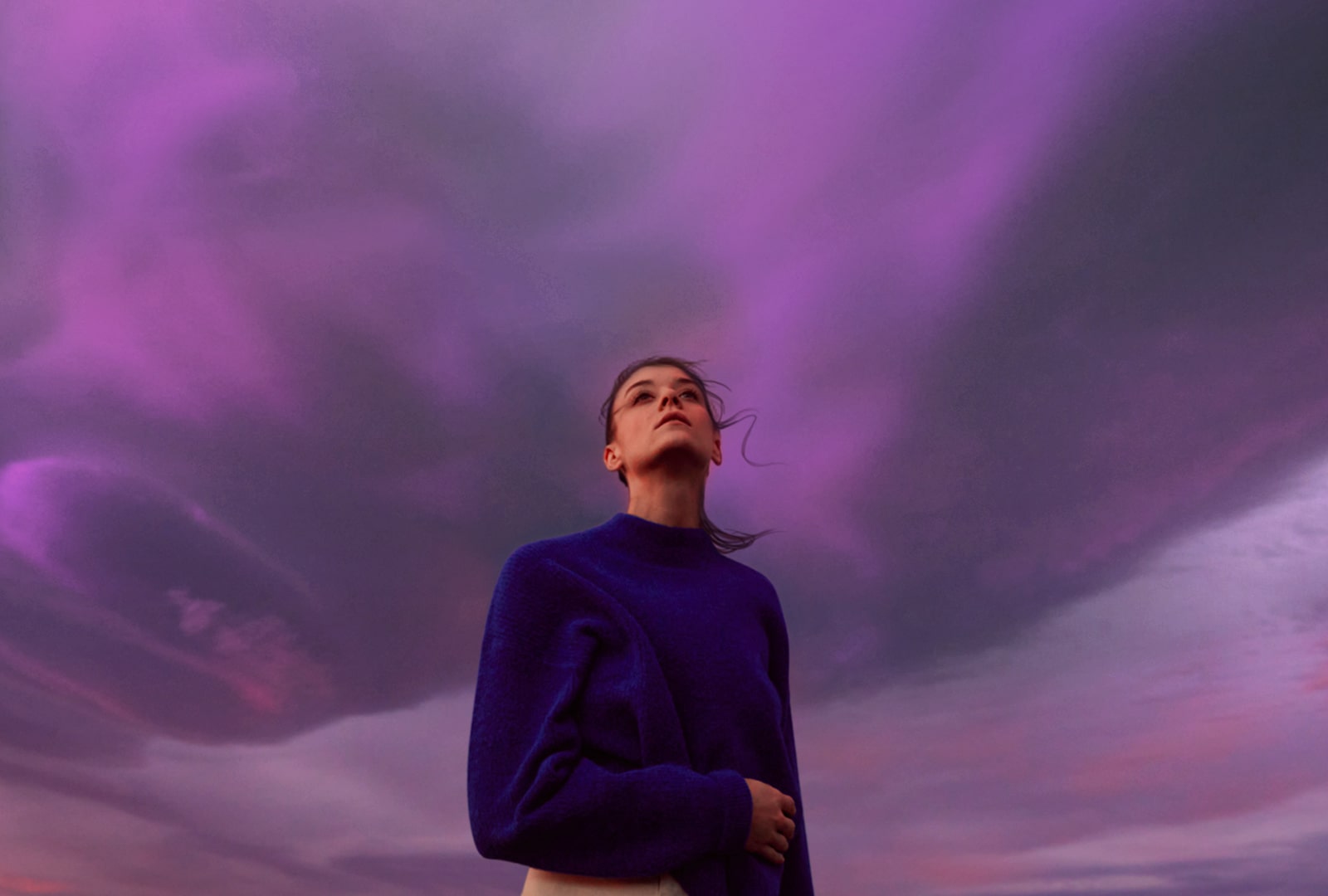 A woman looks at a purple sky. Her hair flutters slightly.