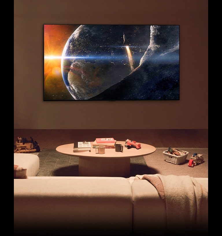 A family sat on the floor of a low-lit living room by a small table, looking up at an LG TV mounted on the wall showing the Earth from space.