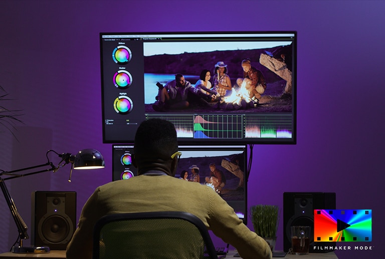 Imagen de un hombre usando dos monitores para editar los colores de una imagen de un grupo de amigos haciendo una fogata.