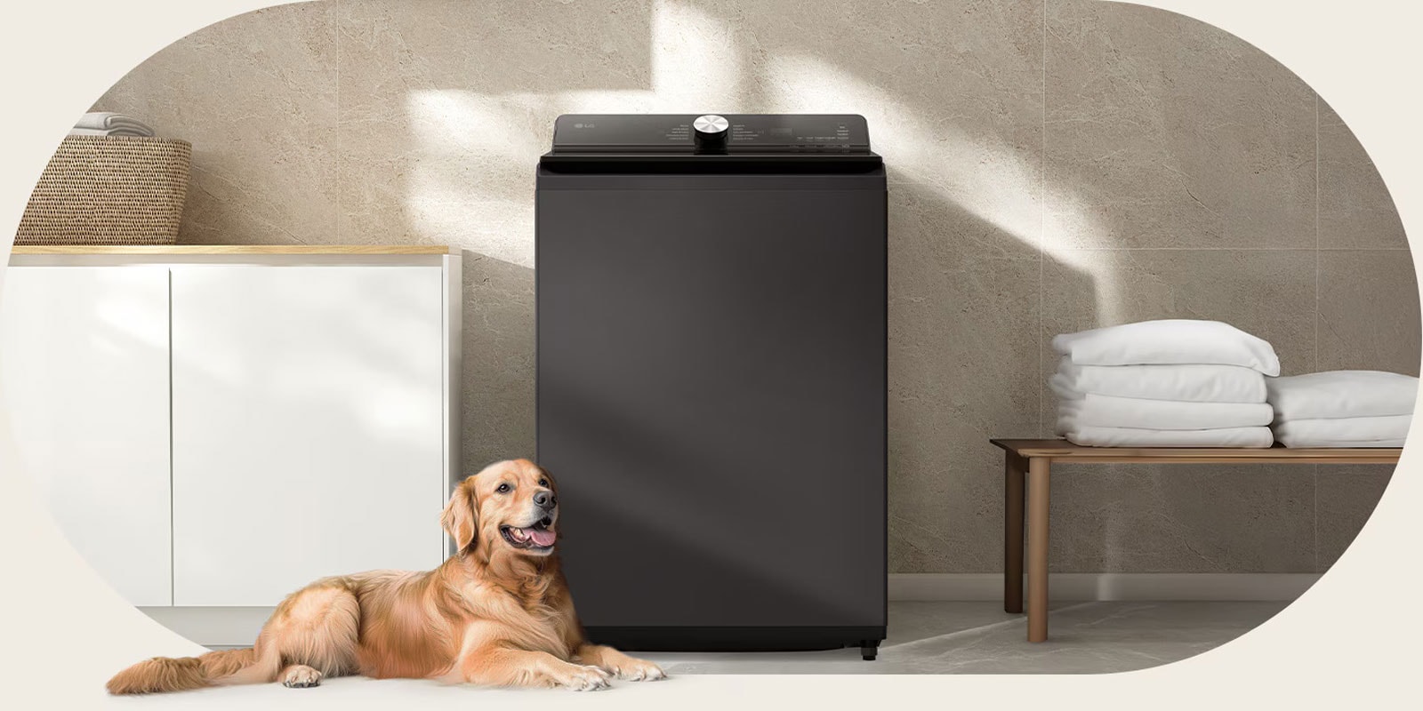 Un perro acostado en el piso junto a una lavadora de carga superior gris oscuro en un espacio de lavandería tranquilo y minimalista con toallas dobladas en un banco.