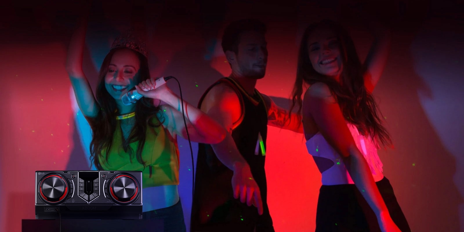 La imagen muestra una fiesta con luces de neón rojas. La gente disfruta de la música; uno de ellos sostiene un micrófono mientras los otros dos bailan. En el lado izquierdo de la imagen hay una mesa con un receptor colocado encima.