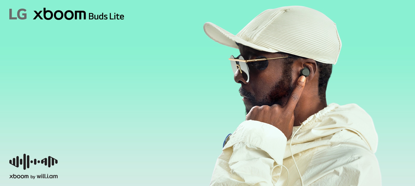 will.i.am con traje blanco y gafas de sol está mirando hacia el lado derecho apuntando el auricular a su oreja con su dedo índice izquierdo.
