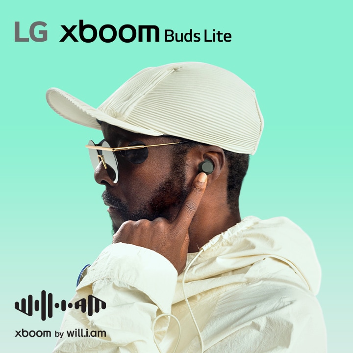 will.i.am con traje blanco y gafas de sol está mirando hacia el lado derecho apuntando el auricular a su oreja con su dedo índice izquierdo.