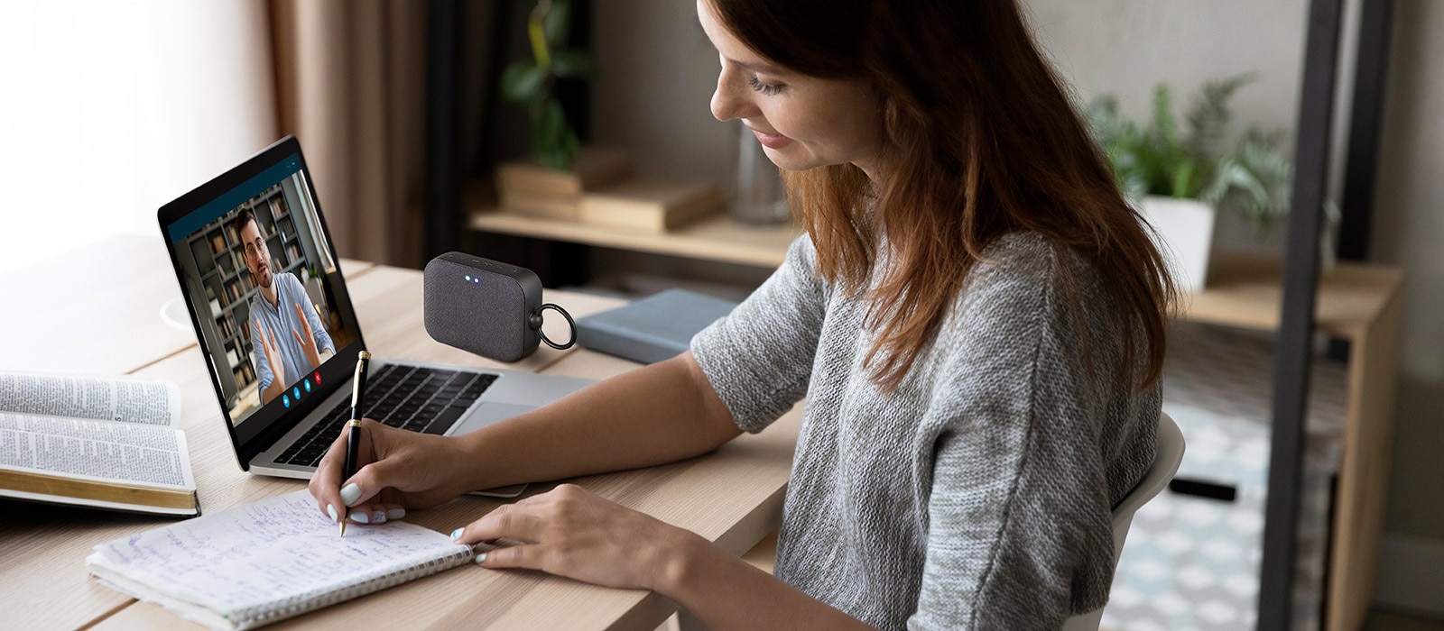 Una mujer en una videoconferencia con un compañero de trabajo, escribiendo una nota al mismo tiempo. El altavoz XBOOM Go PM1 se coloca sobre un escritorio.