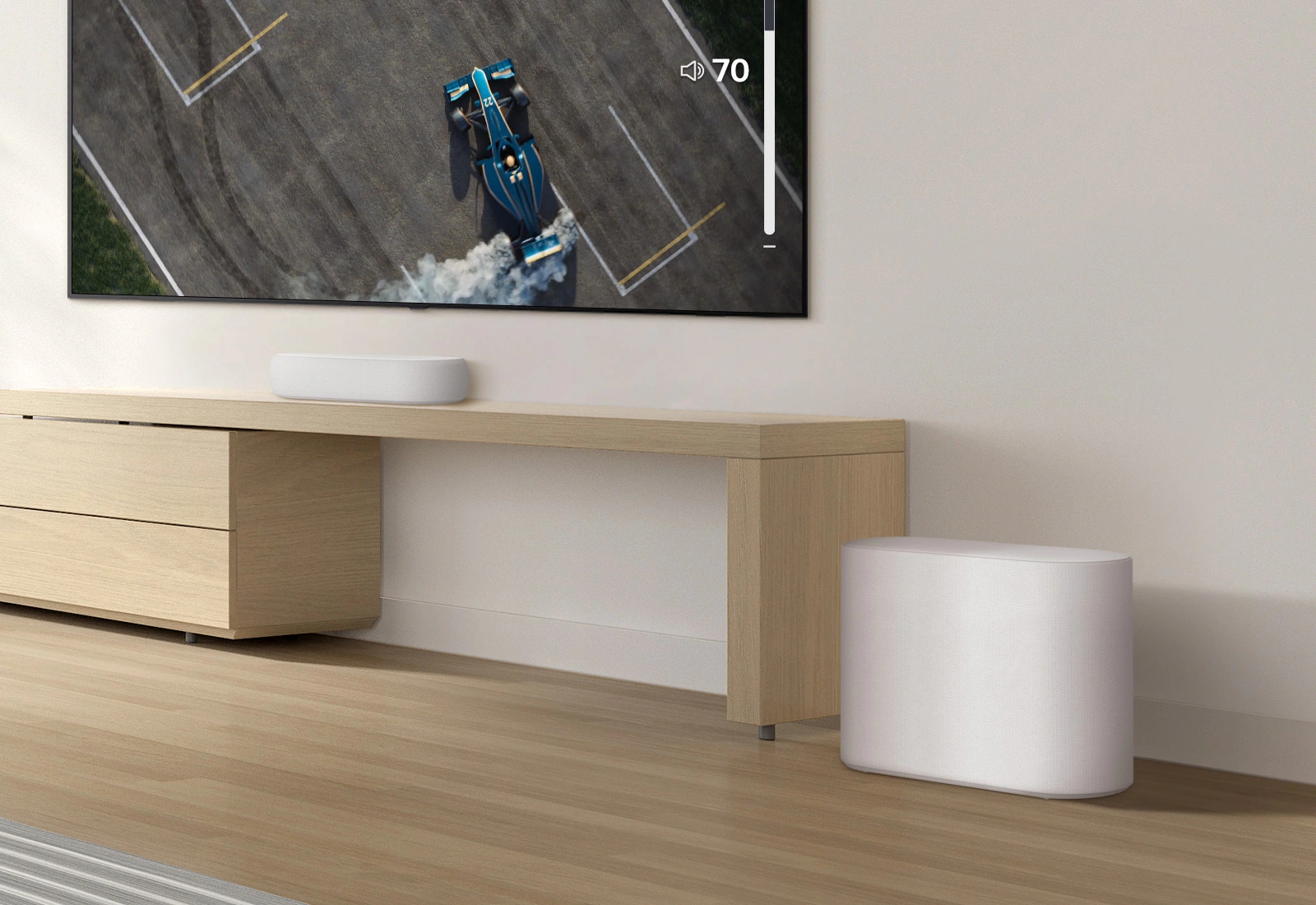 Una barra de sonido se coloca sobre una mesa de madera, un subwoofer se coloca en un piso de madera. Un suave efecto de onda de sonido sale del subwoofer en el suelo. Hay un televisor colocado encima de una barra de sonido. Un coche de carreras en la pantalla de un televisor se conduce muy rápido y violentamente y la GUI del volumen del televisor aumenta.