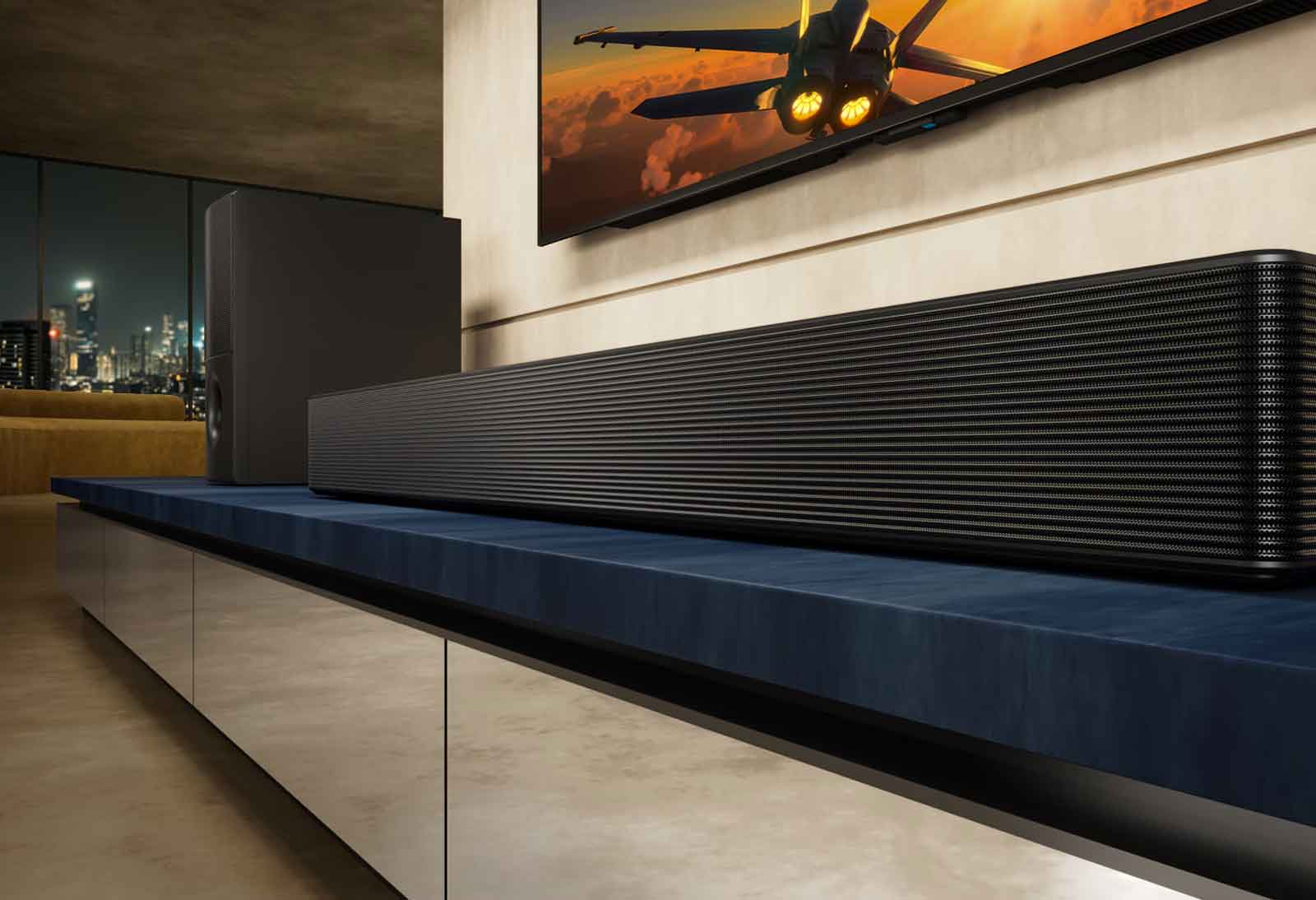 La barra de sonido LG SH5A y su subwoofer se encuentran sobre un mueble de televisión azul en una sala de estar. El televisor con la imagen de un avión se muestra parcialmente sobre la barra de sonido.