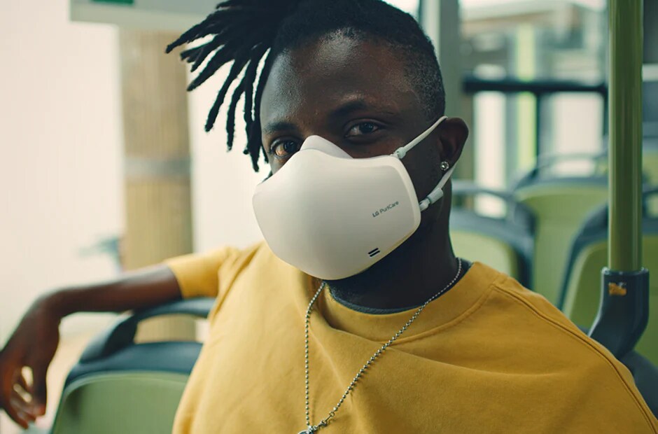 Un hombre afroamericano está sentado dentro de un bus mirando hacia adelante y lleva puesto el purificador de aire facial LG PuriCare™.