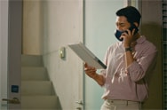 Un hombre asiático sostiene un documento y habla por teléfono. Lleva puesto un purificador de aire facial LG PuriCare™ negro.